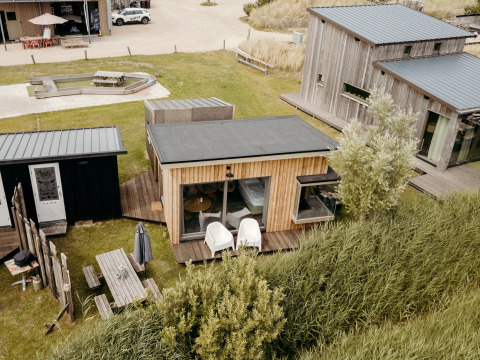 Luftfoto af Solglimt 4 Pers. lodge med træfacader, terrasser og grønne omgivelser nær stranden.