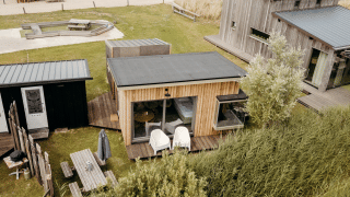 Luchtbeeld van de Solglimt 4 Pers. lodge met houten gevels, terrassen en grasrijke omgeving bij duinen.