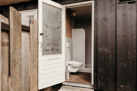 Foto di un bagno di una lodge con porta aperta, wc sospeso e pareti esterne in legno scuro.