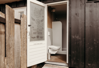Et billede af en lille udendørs badeværelsesindgang på en lodge med en åben dør og toilet synligt.