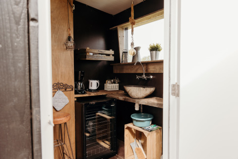 Klein en knus lodgekeukentje met houten planken, stenen wasbak, keukengerei en natuurlijk licht.