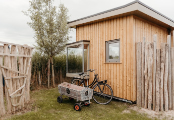 Foto di una casetta in legno presso un lodge con bicicletta e carretto, circondata da una staccionata rustica.