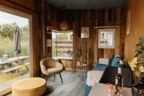 Bright, cozy Solglimt 2 Pers. lodge at Duynpark Het Zwanenwater featuring wood walls, sofa and outdoor view.
