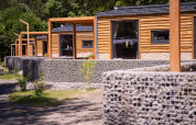 Houten chalets en stenen muren bij Panorama Lodge, Pressegger See, Oostenrijk, in groene omgeving.