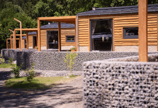 Chalets en bois et murs en pierre à Panorama Lodge, Pressegger See, Autriche, entourés de verdure.