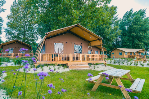 Outdoor photo of Lodgetent Haven 4 safari tent with a wooden deck and picnic table surrounded by greenery.
