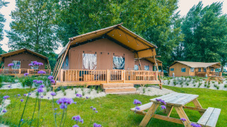 Outdoor photo of Lodgetent Haven 4 safari tent with a wooden deck and picnic table surrounded by greenery.