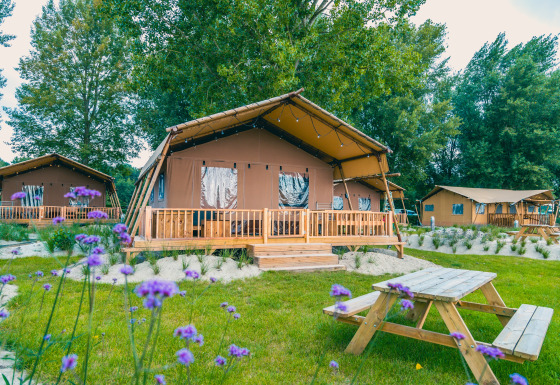 Outdoor photo of Lodgetent Haven 4 safari tent with a wooden deck and picnic table surrounded by greenery.
