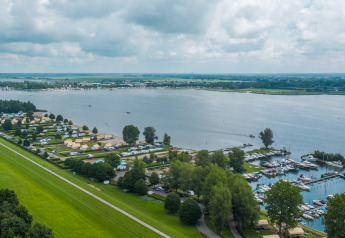 Udsigt over Zuiderzee i Holland med safari telte, campingplads og lystbådehavn under en overskyet himmel.
