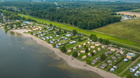 Aerial view of safari tents and campsites along the sandy Zuiderzee beach, bordered by forest and fields.