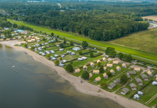 Aerial view of safari tents and campsites along the sandy Zuiderzee beach, bordered by forest and fields.