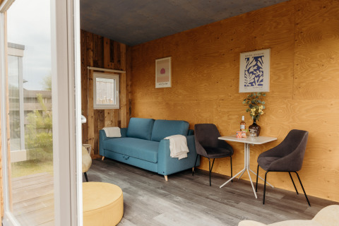 Cozy lodge interior with a blue sofa, wood-paneled walls, table and chairs at Duynpark Het Zwanenwater.