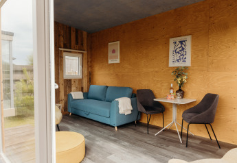 Interno lodge accogliente con divano blu, pareti in legno, tavolo e sedie a Duynpark Het Zwanenwater.