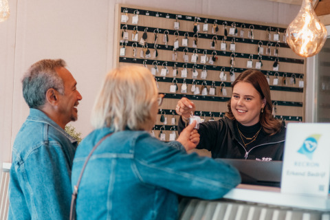 Una recepcionista sonriente entrega llaves a dos huéspedes durante el check-in en un alojamiento glamping.