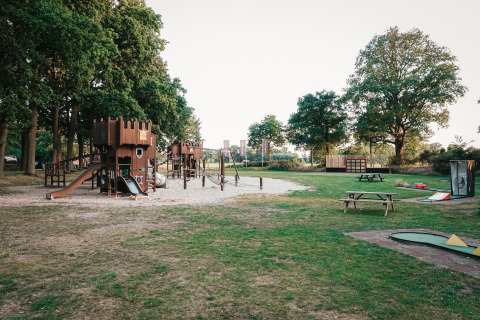 Parque infantil en un alojamiento glamping con castillos de madera, toboganes y mesas de picnic.
