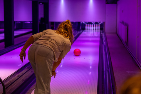 Persona jugando bolos en una pista iluminada de púrpura en un alojamiento glamping, bola avanzando.