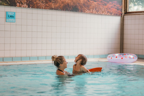 Madre e hijo disfrutan nadando en la piscina cubierta de un alojamiento glamping, con flotador al fondo.