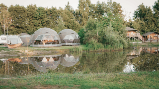 Ronde Holly tenten aan een vijver met weerspiegeling, omgeven door bomen en een ontspannen natuursfeer.