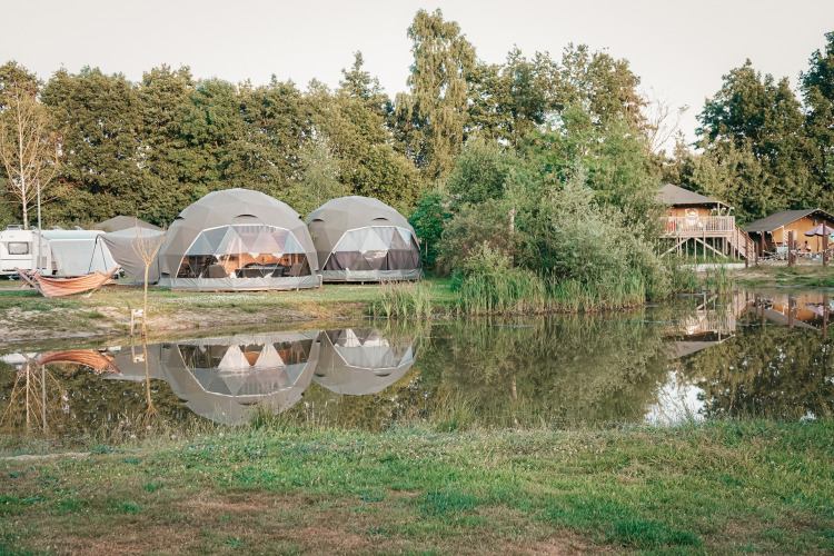 Tiendas Round Holly junto a un estanque que refleja las tiendas, rodeadas de árboles y ambiente relajante.
