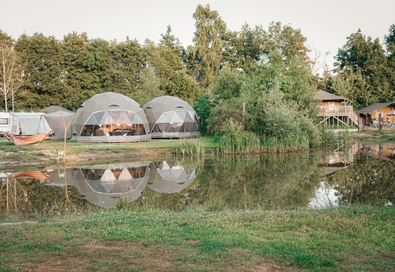 Tiendas Round Holly junto a un estanque que refleja las tiendas, rodeadas de árboles y ambiente relajante.
