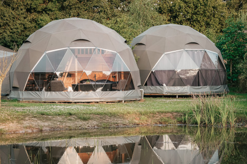 Dos tiendas glamping redondas en Holiday Park Sallandshoeve, Países Bajos, junto a un estanque tranquilo.