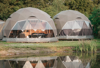 Dos tiendas glamping redondas en Holiday Park Sallandshoeve, Países Bajos, junto a un estanque tranquilo.