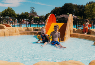 Twee kinderen glijden van de glijbaan in het kinderbad van vakantiepark De Boshoek, Gelderland.