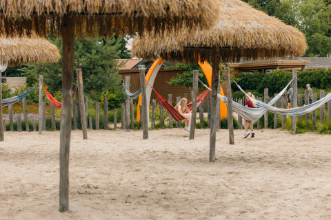 Familievriendelijke plek met hangmatten en rieten daken op zand bij vakantiepark De Boshoek, Gelderland.