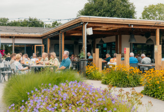 Außenbereich des Restaurants im Ferienpark De Boshoek mit Gästen, Blumen und entspannter Atmosphäre.