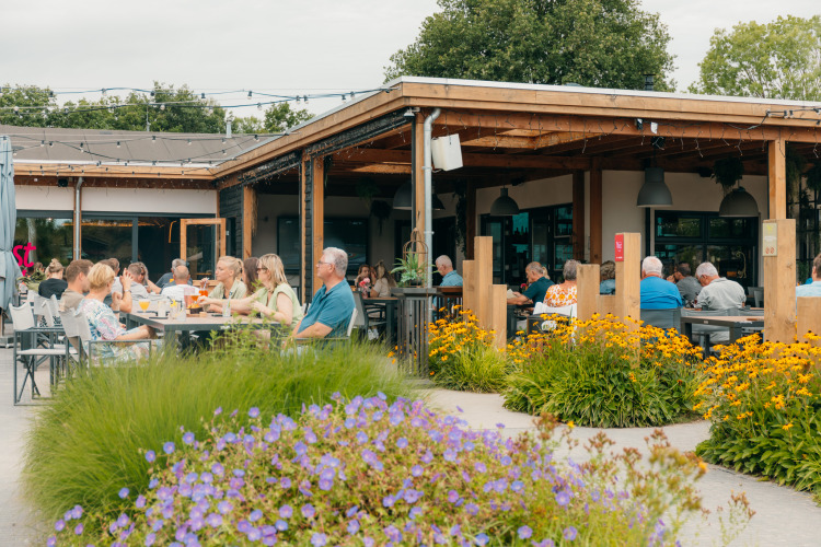 Outdoor dining area at Holiday park De Boshoek in Gelderland with guests, flowers and a relaxed vibe.