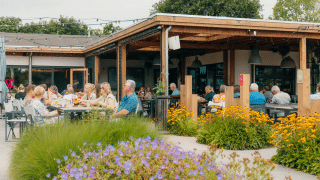 Zona de comedor al aire libre en Holiday park De Boshoek, Holanda, con flores y gente disfrutando.