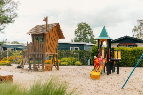Bambini giocano su un parco giochi con scivolo e casetta in legno al De Boshoek, Gelderland, Paesi Bassi.