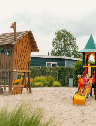 Niños jugando en un parque infantil con tobogán y casa de madera en De Boshoek, Gelderland, Países Bajos.