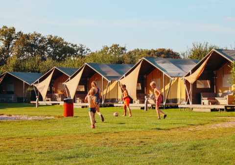 Kinder spielen Fußball vor luxuriösen Zelten im Ferienpark De Boshoek in Gelderland, Niederlande.