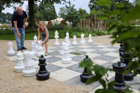 Un enfant et un adulte jouent aux échecs géants sur un échiquier extérieur dans un parc de vacances glamping.