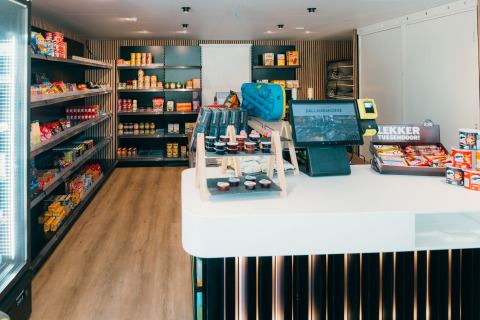 Un mini-marché moderne dans un parc de vacances glamping, étagères avec snacks et caisse à l’avant.