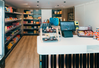 Un mini-marché moderne dans un parc de vacances glamping, étagères avec snacks et caisse à l’avant.