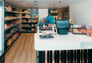 Een moderne minimarkt op een glamping-vakantiepark met snackschappen en een kassa op de voorgrond.