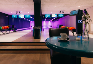 Bowlingbahn mit leuchtenden Lichtern, Kaffeetasse auf Tisch und bunte Kugeln im Hintergrund.