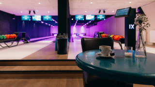 Bolera interior con bolas de colores, pantallas electrónicas y una taza de café sobre una mesa azul.