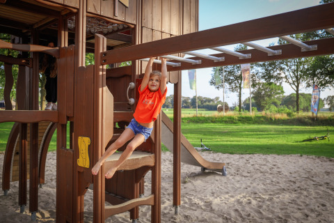 Enfant jouant aux barres sur un terrain de jeu sablonneux d’un parc de vacances avec glamping.