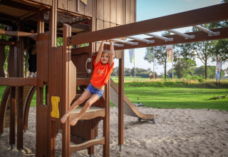 Enfant jouant aux barres sur un terrain de jeu sablonneux d’un parc de vacances avec glamping.