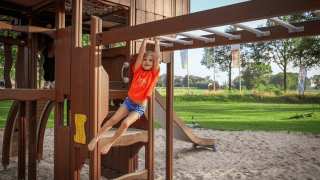 Niña juega en columpios de parque infantil con arena en parque vacacional con alojamiento glamping.