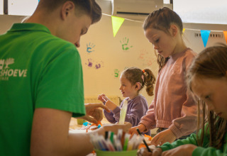Des enfants et un adulte réalisent des activités manuelles dans un parc de vacances, main colorée au mur.