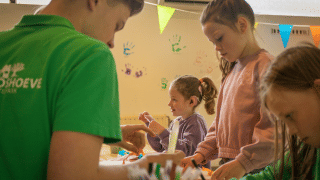 Niños y un adulto hacen manualidades en interiores en un parque vacacional con huellas de manos en la pared.
