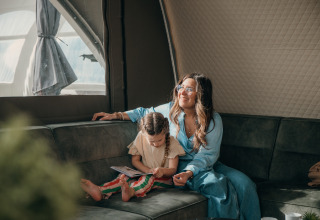 Mère et enfant se détendent dans une tente de glamping au parc de vacances, l'enfant lit sur le canapé.