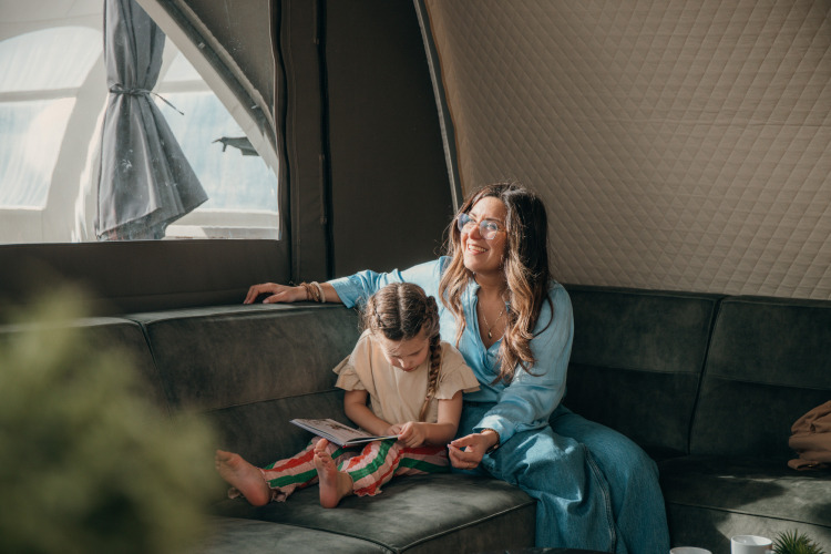 Mutter und Kind entspannen im Glamping-Zelt auf einem Ferienpark, das Kind liest auf dem Sofa.