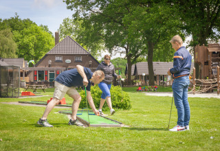 Drei Erwachsene spielen Minigolf in einem Ferienpark mit Glamping-Unterkünften und Spielplatz.