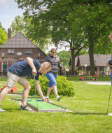 Tres adultos juegan mini golf en un parque vacacional con alojamientos glamping y zona de juegos infantil.