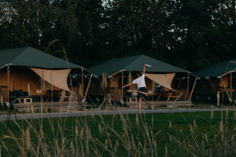Personne jouant au frisbee devant des tentes glamping dans un parc de vacances entouré de verdure.
